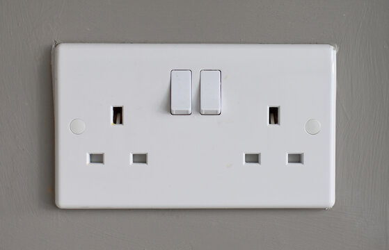 Generic white plastic, double, electric three pin plug socket. Fixed to a mushroom coloured background wall