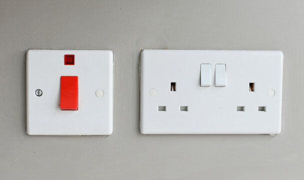 Generic white plastic, double, electric three pin plug socket. Fixed to a mushroom coloured background wall