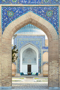 Gur-e-Amir mausoleum entrance arch with blue tilework and muqarnas vault in Samarkand. Ornate Islamic portal framed by brick walls and floral majolica decoration. Ideal for travel guides, heritage.