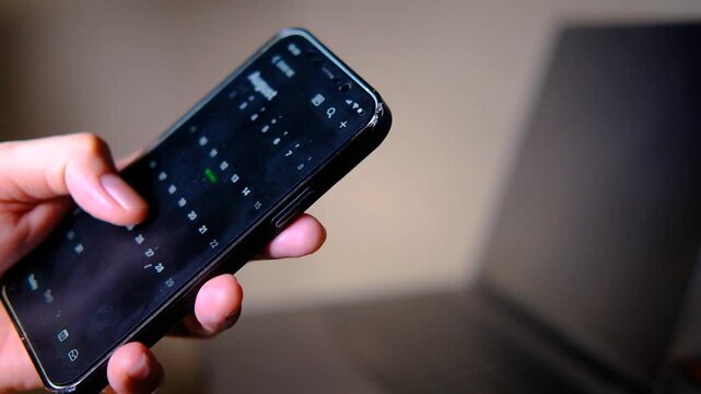 Close-up of a hand scrolling through a holiday calendar on a smartphone with a laptop in the background. Represents vacation planning, annual leave, paid time off (PTO), employee leave management.