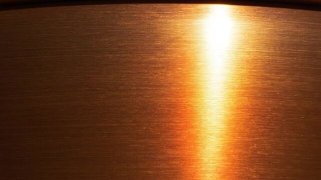 Close-up of a copper surface with a bright light reflecting across horizontal textures, metallic abstract background