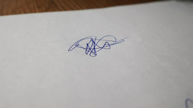 Hand holding an orange ballpoint pen begins to write on a clean sheet of white paper. The shallow depth of field highlights the sharp pen tip as it touches the blank surface.