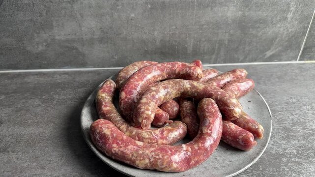 Video of a person's hand arranging raw kupati sausages made from fresh goat meat on a grey ceramic plate in the kitchen, 4k