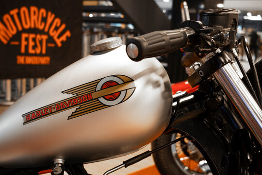 Close-up of a Harley-Davidson custom motorcycle fuel tank, featuring retro graphics, telescopic fork, handlebar controls, and brushed metallic finish.
