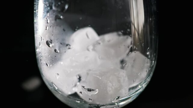 Water droplets and mist slowly condense and trickle down the surface of a chilled glass in slow motion. Concept of refreshment, purity, thirst, hydration, and cold beverage preparation.