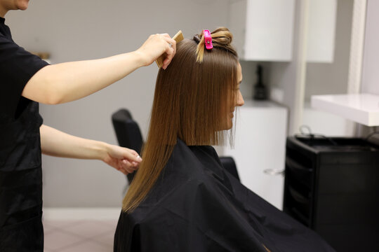 Unrecognisable professional hairdresser ironing female client hair with hair straightener and comb, making stylish hairstyle in beauty salon. Keratin, lamination, hair care, hair salon and hairstyling