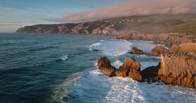 Sintra Cascais Natural Park where Atlantic Ocean waves crashing against the rugged coastline and cliffs during sunset, creating a dramatic and natural landscape. Travel Portugal. Static shot footage