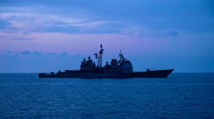 Fototapeta premium Silhouetted warship glides across calm ocean waters