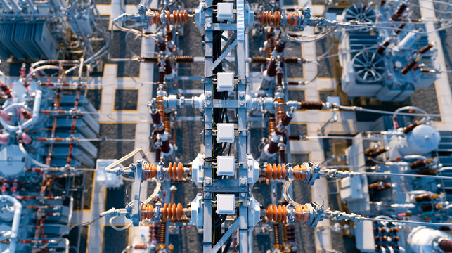 Aerial view gliding over an array of electrical components of a substation busbars switches and transformers in geometric patterns bright midday light aerial view electrical
