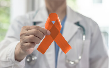 Obraz na płótnie Canvas Orange ribbon for Leukemia, kidney cancer awareness month, multiple sclerosis, lupus, ADHD illness, self-injury and Appendix Cancer with amber color bow on doctor's hand