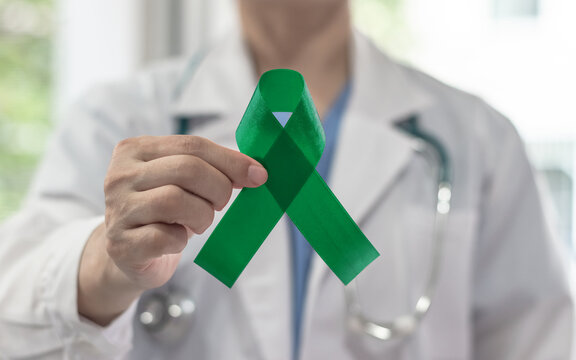 Green ribbon for gallbladder and bile duct cancer awareness month in February, adrenal cancer, Leukemia, bipolar disorder, mental health illness with kelly green bow on doctor's hand support