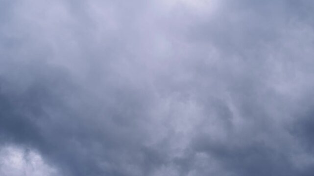 Timelapse shows dense grey storm clouds drifting rapidly with brief blue patches peeking through thick layers. The heavy mist and dark atmosphere suggest an approaching tempest.