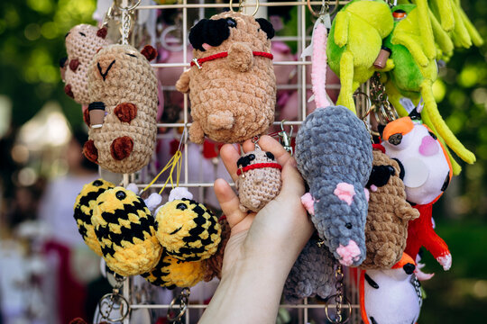Woman choosing handmade plush animal keychain at craft market.