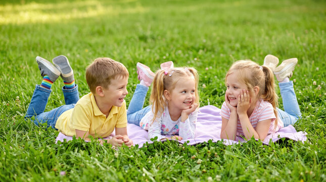 Three kids lying on grass laughing together, Friendship Day concept, happy children relaxing on a blanket outdoors in a sunny park, best friends bonding, childhood joy and playful summer moment