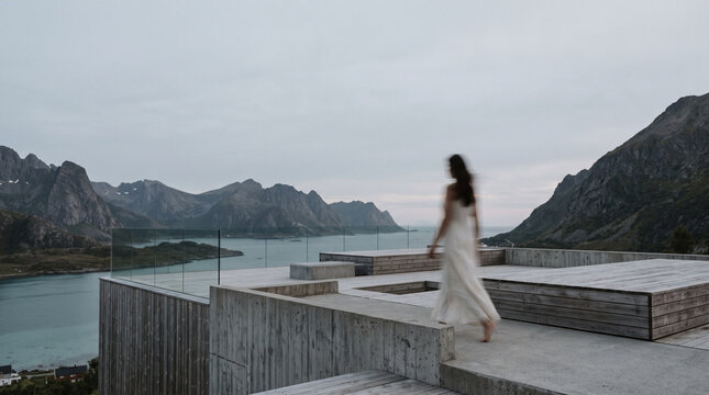 Woman in White Dress Walking on Modern Terrace Overlooking Mountain Lake