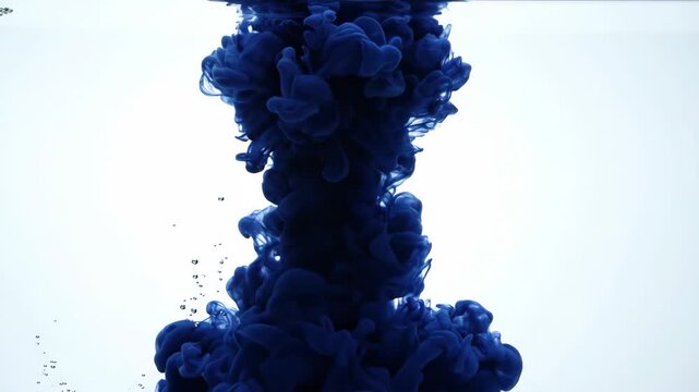 Dark blue ink dissolving and spreading in water on light background for creative and artistic content