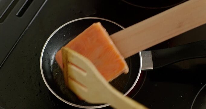 Flipping salmon fillet in frying pan using wooden spatulas
