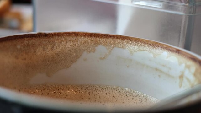 Macro slow motion shot tracking the thick brown foam ring stain left on the inner rim of a white ceramic cappuccino cup as it tilts.

