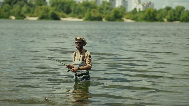 Fisherman Stands In River Water Holding Spinning Rod. Summer Hobby. Sport Angling 
