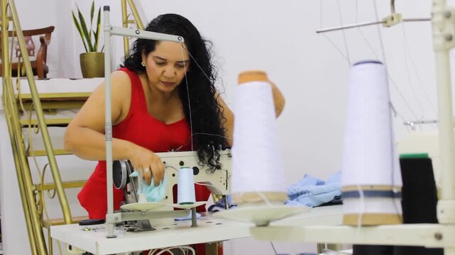A Colombian seamstress is dusting her sewing machine and table to begin the clothing manufacturing process in a sewing studio in Neiva, Huila, Colombia. Concept of small business and independent