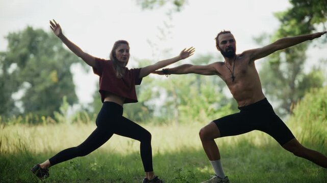 People Practicing Yoga In Warrior Pose On Green Grass Field. Meditation. Stretching