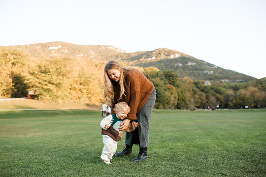 Happy woman having fun with her little baby girl in green grass lawn and mountain landscape at background. Motherhood.