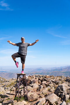 White male posing on the peak of Cerro Tres picos mountain peak marker, standing on one leg, yoga