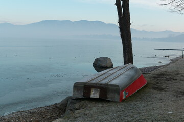 Fototapeta premium Upside-down wooden rowboat on a tranquil lakeshore with misty mountains in the background