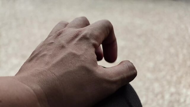 Slow motion video capturing a stressed male hand rhythmically tapping fingers against his knee, showing signs of nervousness, panic attack, or deep worry.
