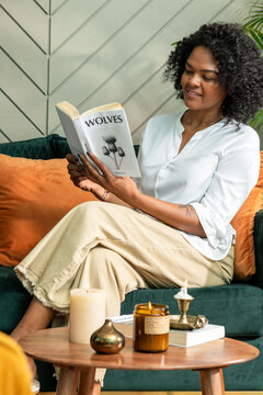Woman reading a book on a cozy couch with candles and decor.