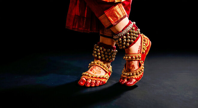 Indian Classical Dance Feet: A close-up captures the intricate footwork and adornments of an Indian classical dancer, showcasing traditional anklets and vibrant red attire against a dark.