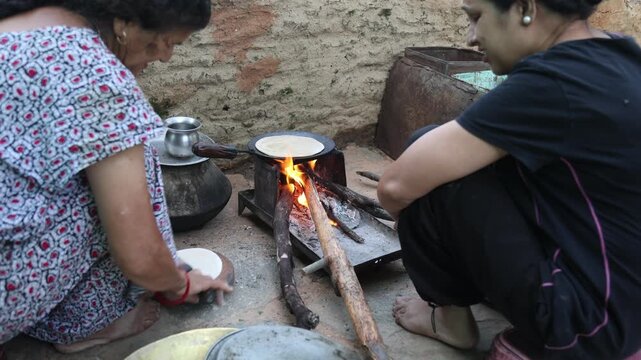 Raw video footage of two village women making traditional roti on a wood-fired stove in Uttarakhand, India, showcasing authentic rural cooking, village life, and poverty.