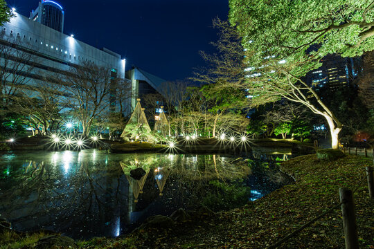 Wide-angle night view of Koishikawa Korakuen with magical light flares and Yukitsuri reflecting on the pond January 2024