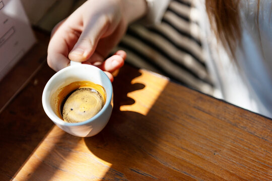 Close-up of a hand holding an espresso cup on a wooden table.
