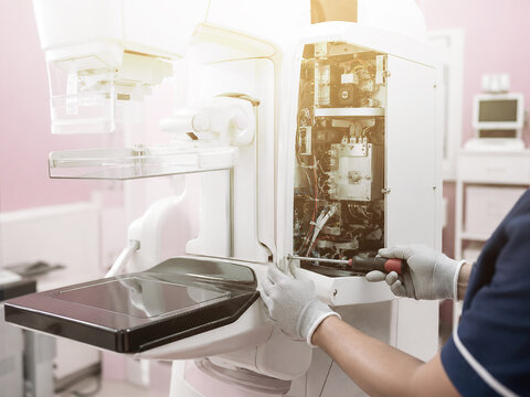 Technician repairing mammography machine with open panel