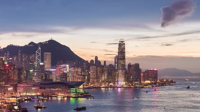 Asia, China, Hong Kong, day to night transition time lapse of Hong Kong's financial district and skyline at sunset, with Victoria Bay with passing boats in foreground.