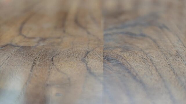 Slow motion shallow depth of field video showcasing the natural grain, polished texture, and warm brown pattern of a classic wooden table top surface.
