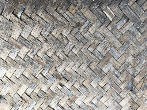 A traditional Indonesian bamboo weaving pattern known as turi. The texture of the woven fabric is dirty and aged, with natural pieces interwoven in a herringbone pattern. The abstract background featu