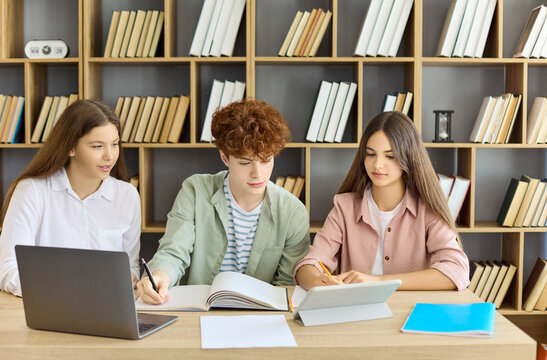Students collaborate in library using laptop and tablet. Teamwork and collaboration guide study and learning on a class project in a bright classroom for education. Teamwork and study theme shown.