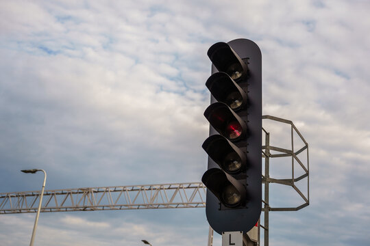 Vertical railway signal light showing a red indication against a cloudy blue sky, representing transportation safety and track control, train transport safety, stop and wait signalization