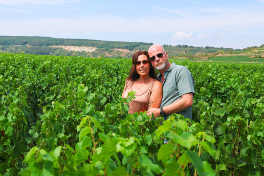   
Couple standing among lush chardonnay vines in Puligny‑Montrachet near Beaune, Burgundy wine region of France on a sunny summer day.