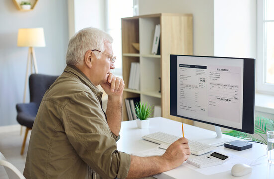 Senior man reviewing invoice on computer. At home he uses a calculator to plan finance for utilities and monthly bills, checking details and deadlines. Strong concept of on time payment.
