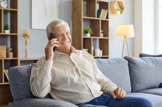 Senior man smartphone talking home sofa indoors. Relaxed retired adult enjoys mobile conversation, showing family connection and modern communication. Concept: senior connection at home.