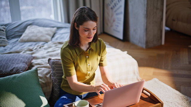 Morning lady texting laptop pressing buttons sitting bedroom in sun rays closeup