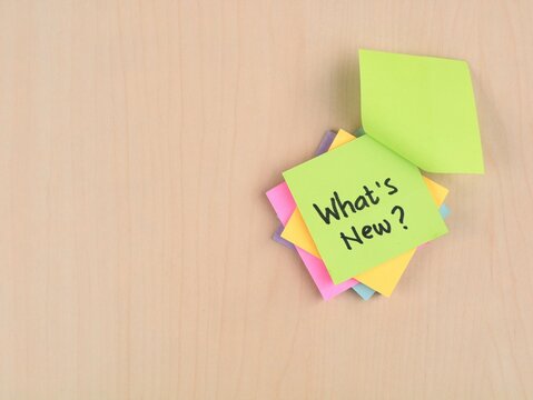 What's New? text handwritten on colorful adhesive notes on wooden desk with copy space. Ideal for business updates, marketing announcements, latest trends, or news presentation