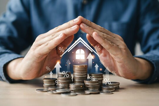 Hands protecting a house icon over coins. Real estate insurance and mortgage growth concept.