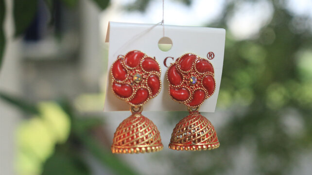 Pair of red traditional indian jhumka earrings hanging on display card with gold plated jewelry making traditional wear earrings accessories ornaments adornment bijouterie