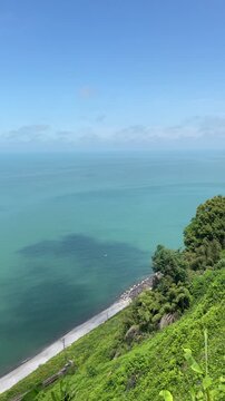 sunlit turquoise sea stretches along a lush green cliffside with a quiet narrow beach below, creating a peaceful coastal travel landscape under a clear expansive blue sky