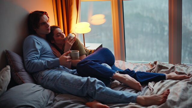Late couple cuddling together sipping hot tea in bedroom. Family holding coffee