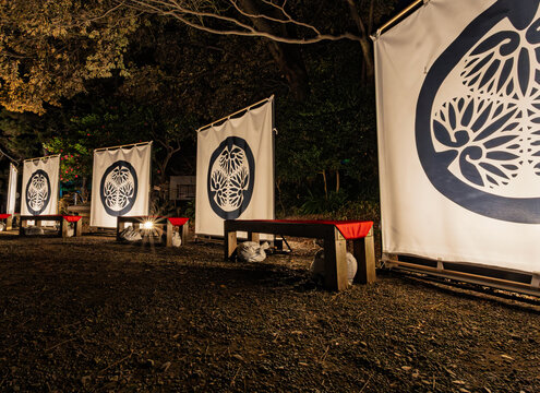 Banners with the Tokugawa clan crest and red-covered benches illuminated at night in Koishikawa Korakuen January 2024